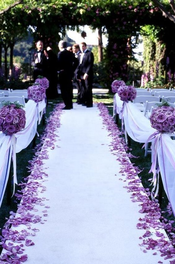 Pomanders of purple roses, scattered petals and purple satin ribbons line the aisle of this outdoor wedding ceremony