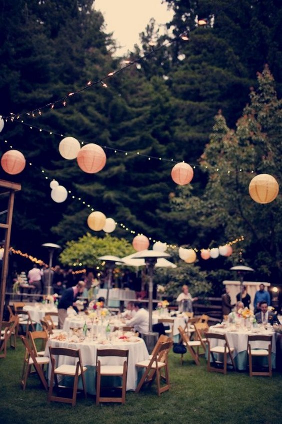 outdoor wedding reception tissue puff balls hanging on string between trees in the backyard.