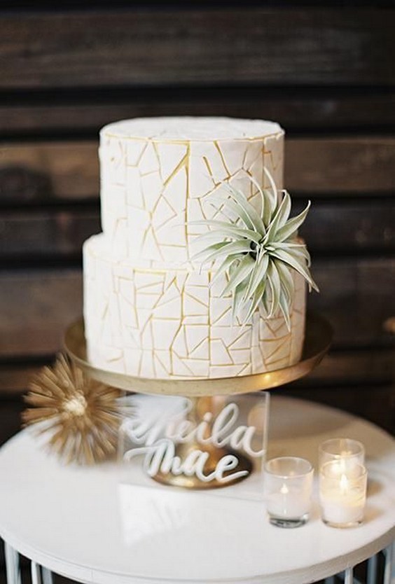 two-tiered white-and-gold wedding cake with geometric details and decorated with an air plant by danielle keene