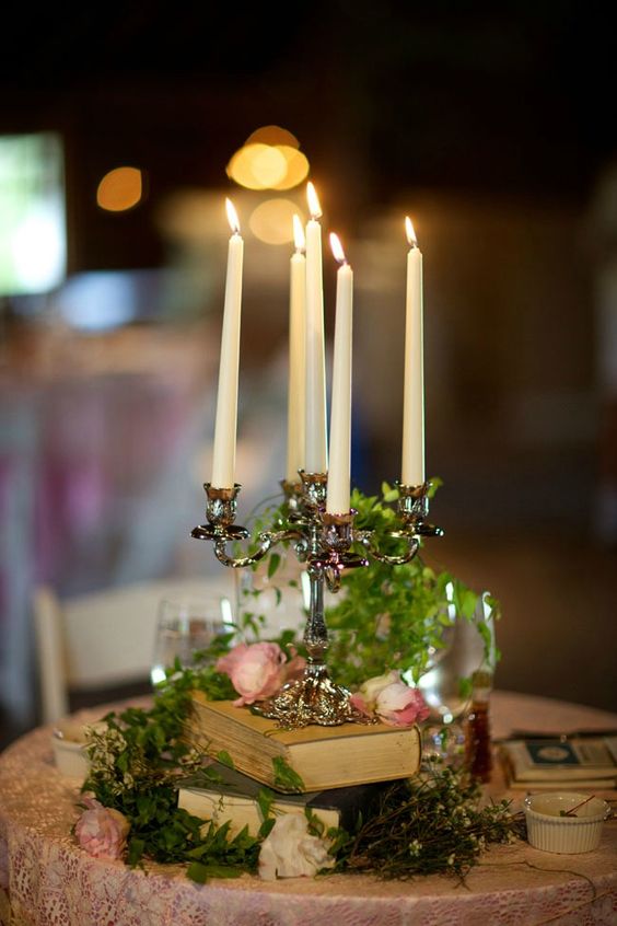 Mixed matched candelabra centerpieces stacked on vintage books with draped green vine & blooms