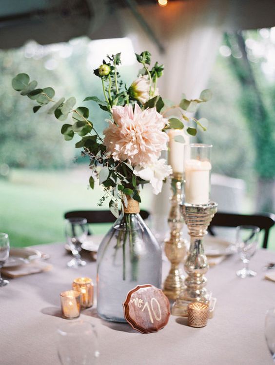 wedding centerpiece use glass bottle and accompany with varied candlesticks and votive candles
