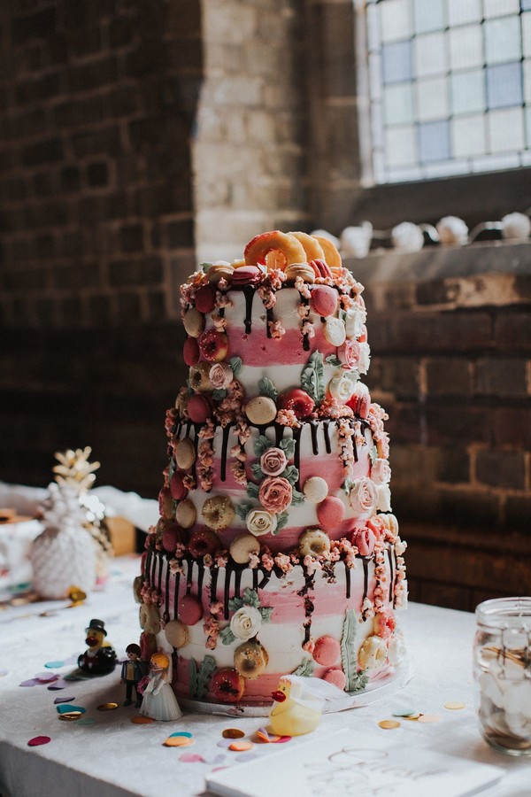 Three tier white and blush chocolate drip cake decorated with macarons, doughnuts and sugar flowers