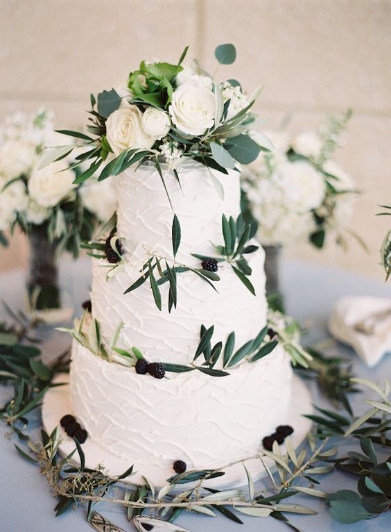 Simple Elegant Wedding Cake with Olive Leaves and White Flowers on a Wooden Cake Stand