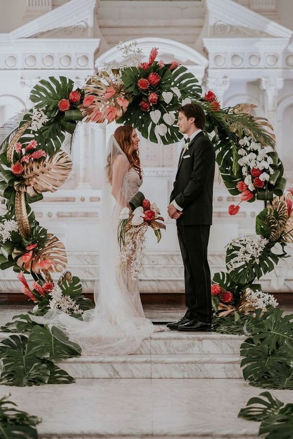tropical wedding arch with gilded monstera leaves, white orchids and king proteas