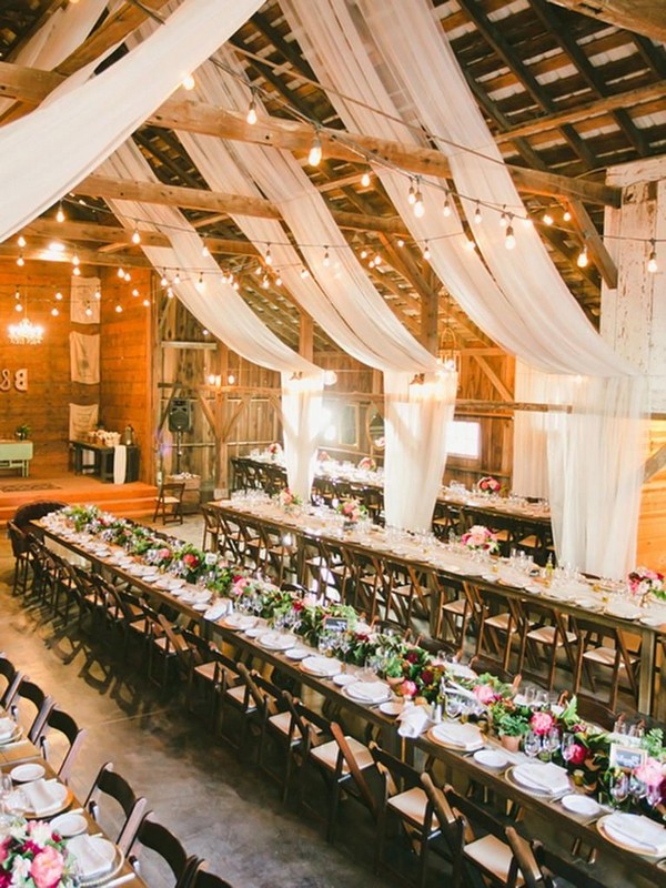 Rustic barn wedding reception space with draped white fabric decor